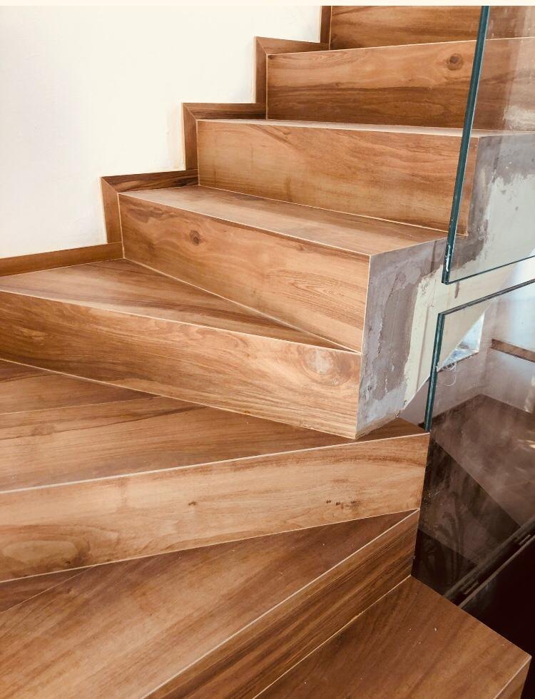 Primo piano dei gradini di una scala rivestiti in gres effetto legno, con pedata e alzata dello stesso materiale e un parapetto in vetro